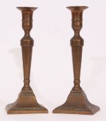Pair of bronze or cast metal candlesticks, moulded stems and spreading square bases, the bases