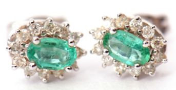 Pair of 18ct white gold, emerald and diamond cluster earrings, the oval faceted emerald raised