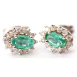 Pair of 18ct white gold, emerald and diamond cluster earrings, the oval faceted emerald raised