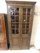 MID-20TH CENTURY OAK FRAMED CABINET WITH GLAZED DOOR OVER PANELLED DOOR WITH CARVED DETAIL