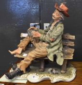 Large Capo di Monte or Naples figure of a tramp seated on a wooden bench, 30cm long