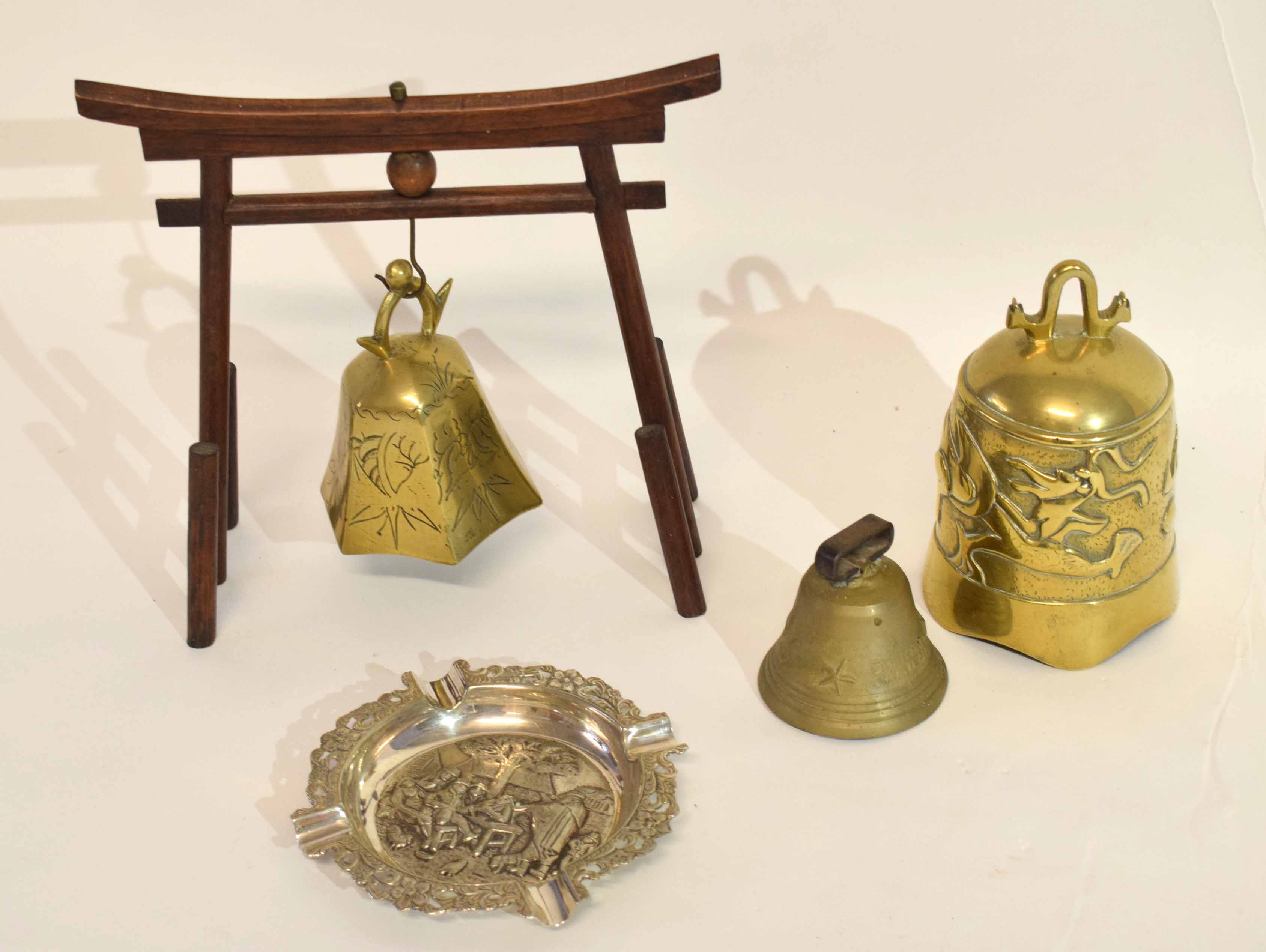 Group of brass bells, one with wooden stand, together with a white metal ashtray impressed with a