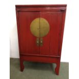Red Chinese style cabinet on raised legs, with large brass plates and carved drop handles on front