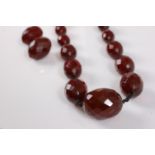 A faux 'cherry amber' bead necklace, the graduated faceted beads knotted on black cord, approx.