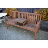 A stained and slatted teak three seater garden bench having, central table platform