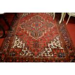 A Persian red ground woollen rug, having stylised geometric floral ground within trailing tramline