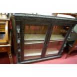 A circa 1900 heavily carved and ebonised oak double door glazed bookcase, width 120cm