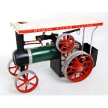 A Mamod live steam traction engine comprising green body with red spoked wheels and a cream canopy