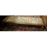 An early 20th century Continental walnut, tapestry embroidered and studded low long footstool,