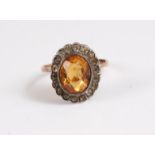 A citrine dress ring, the oval citrine collet mounted and surrounded by small white hardstones,