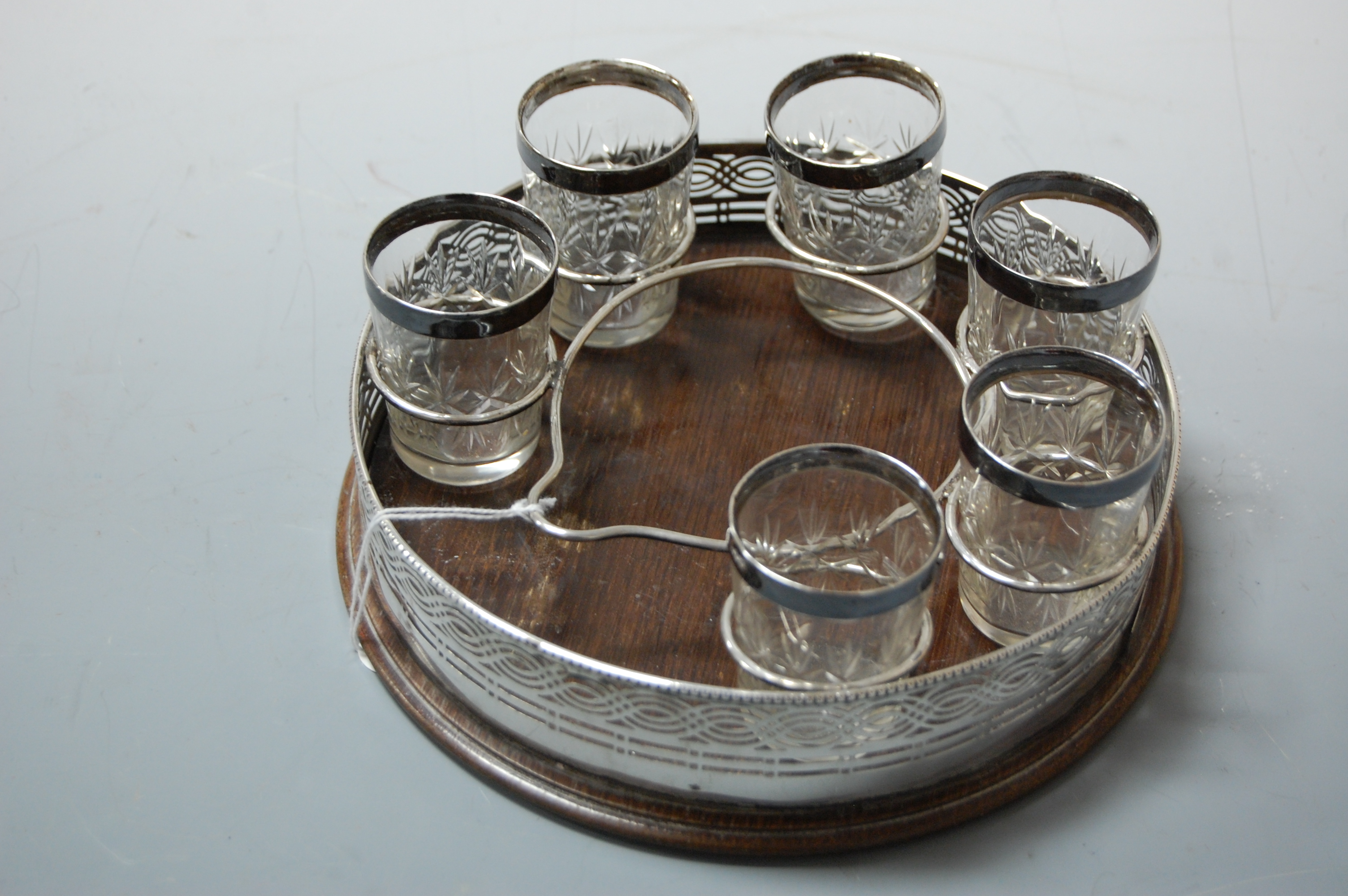 An Edwardian part liqueur set having a pierced silver mounted circular tray on oak base containing