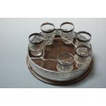 An Edwardian part liqueur set having a pierced silver mounted circular tray on oak base containing