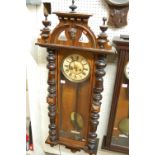 A late 19th century Vienna walnut drop trunk wall clock, having a turned and mask carved top,