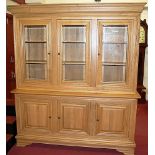 A contemporary joined light oak bookcase cupboard, having three bevelled glazed upper doors with
