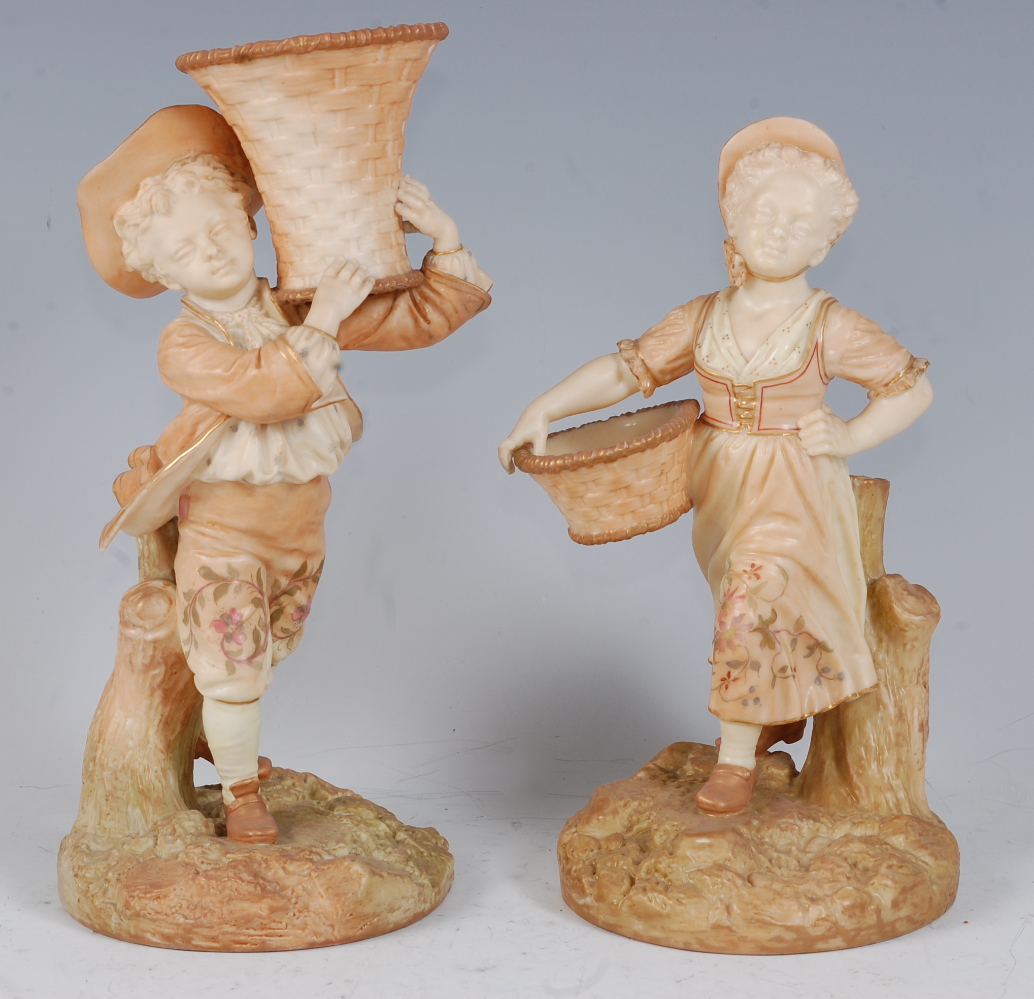 *A pair of Royal Worcester blush ivory figures, the boy in standing pose with a basket upon his