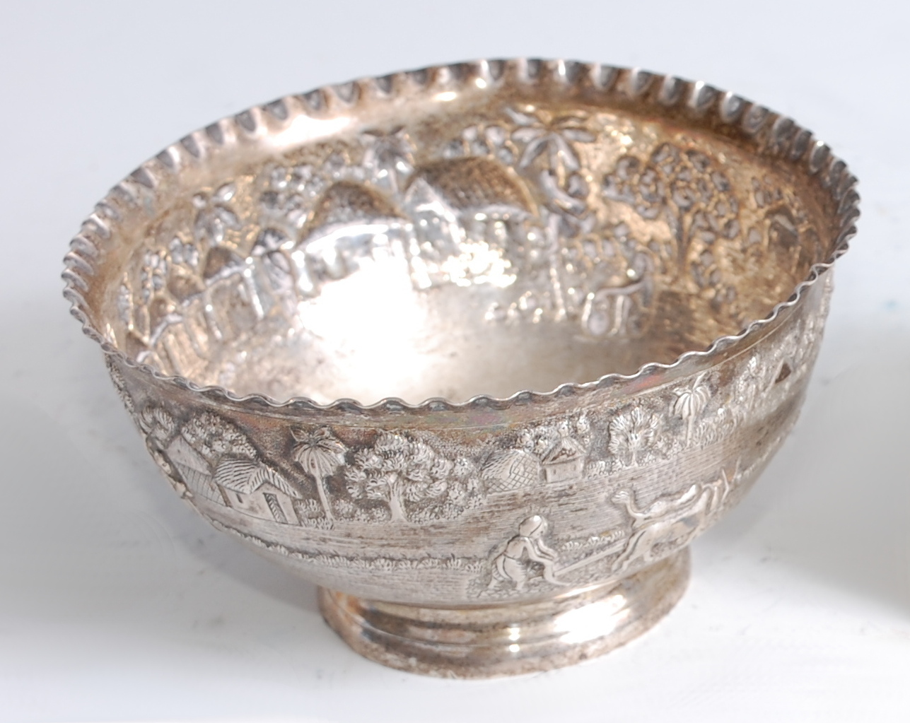 A circa 1900 Chinese white metal bowl, having a wavy rim above an embossed border depicting