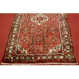 *A Persian woollen red ground rug, having a central medallion and multiple borders, 107 x 170cm