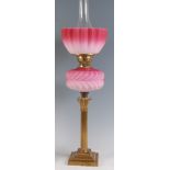 A late Victorian lacquered brass pedestal oil lamp, having pink tinted shade over brass burner and