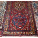 A Persian woollen Heriz runner, the red ground decorated with five medallions within trailing