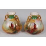 *A pair of Royal Worcester twin handled porcelain vases, of squat melon form, each hand-painted with