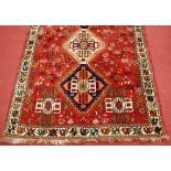 *A Persian woollen rug, the red ground decorated with three linked lozenge medallions, stylised