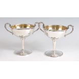 A pair of American sterling silver pedestal cups, each having acanthus leaf capped twin handles