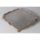 A 1930s silver salver, of shaped square form, with raised scrolling borders and on shell cast