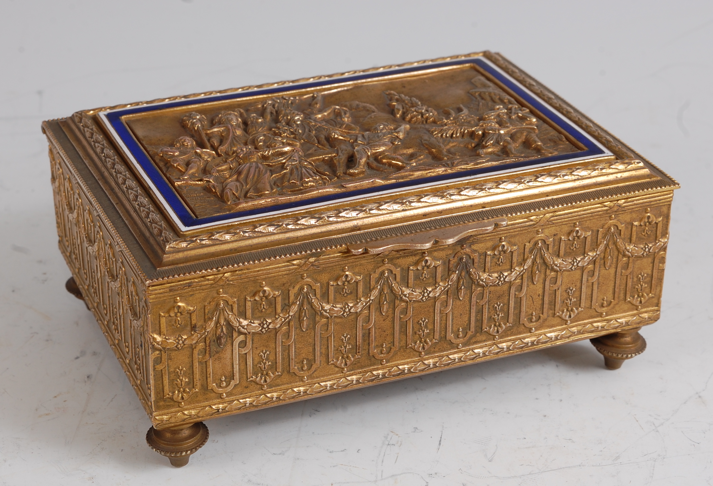 A late 19th century brass music box, the hinged cover cast with a scene of merry-making and