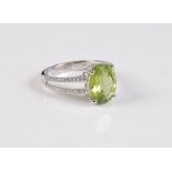 A 14 peridot and diamond ring, the oval peridot, in a four claw mount, with bifurcated half set