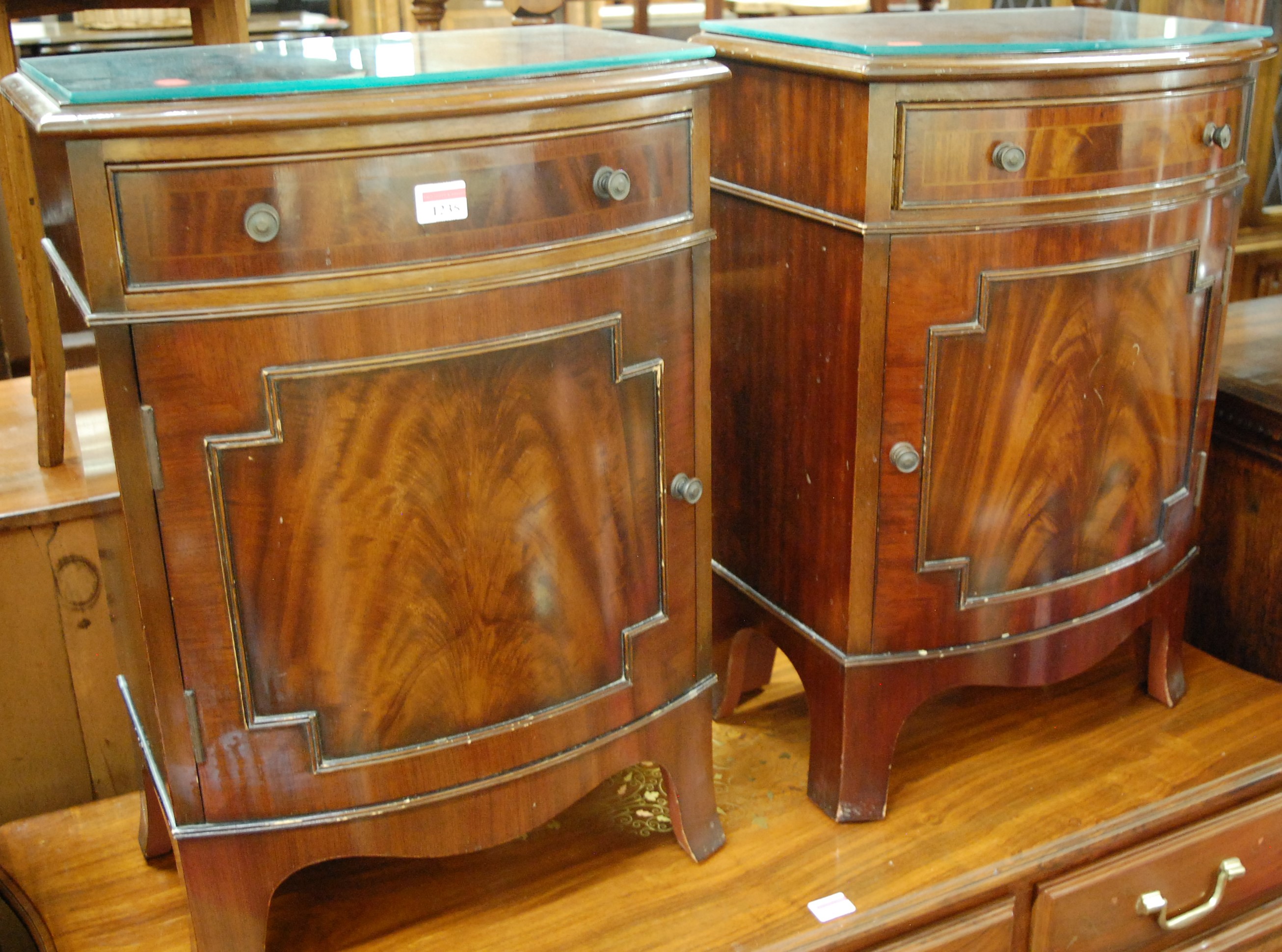 A pair of reproduction mahogany and flame mahogany bowfront single door bedside cupboards, each with