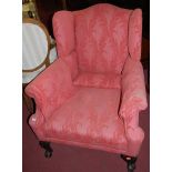 A pair of early 20th century pink floral upholstered wingback scroll armchairs, raised on squat
