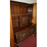 An early 20th century heavily relief carved oak dresser, the upper section with two tier open