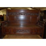 A circa 1900 floral relief carved and further panelled oak three panelled hinged top settle,
