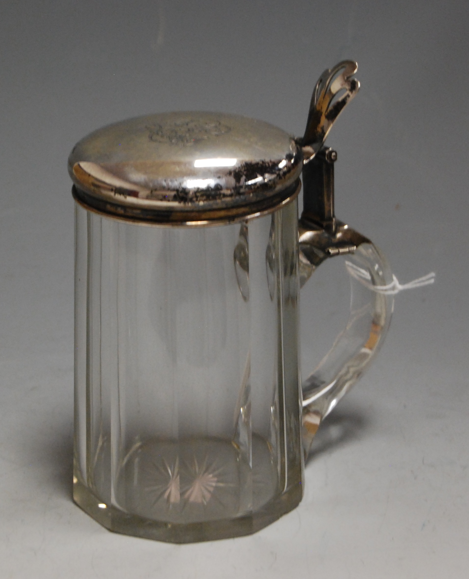 An early 20th century German bierstein having faceted clear glass body with white metal mount with