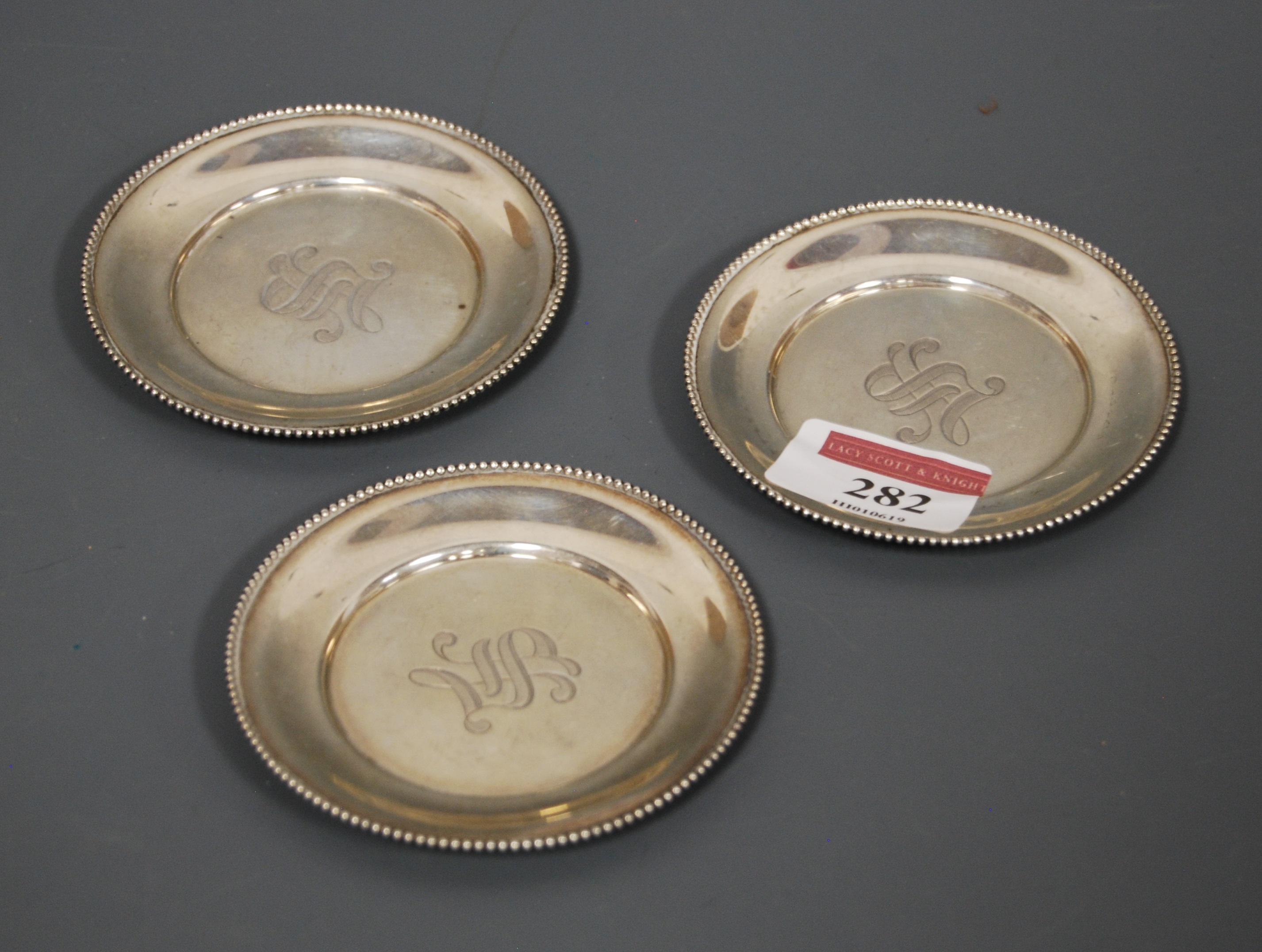 A set of three miniature silver dishes, each having a monogrammed centre within beaded border