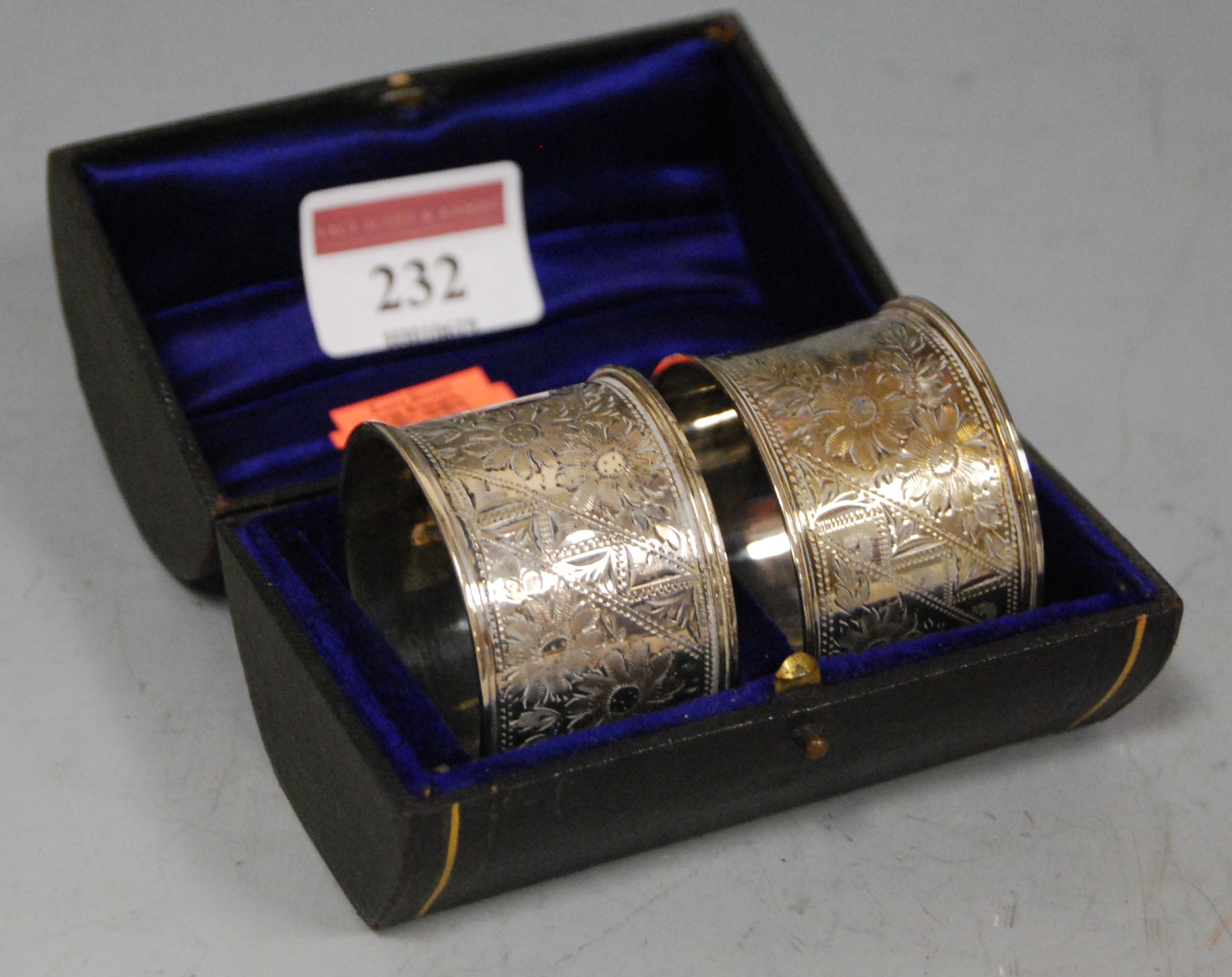 A pair of George V silver napkin rings, each having all-over floral engraved decoration, housed in