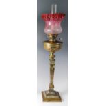 A late Victorian brass pedestal oil lamp, having cranberry tinted and acid etched shade, the brass