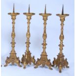 A set of four gilt brass alter sticks, in the Baroque style, having multi-knopped columns to triform