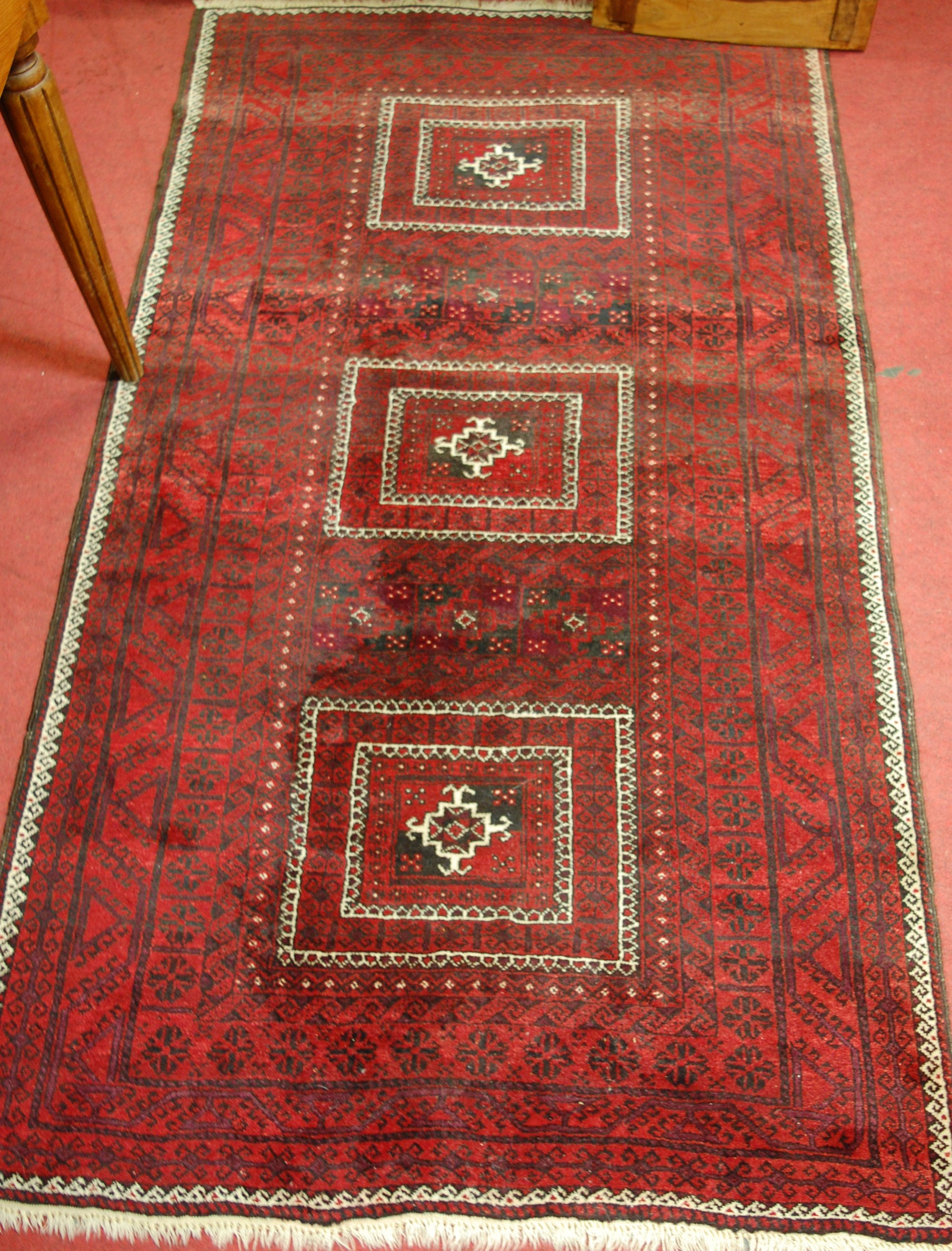 A Persian woollen rug, having a rust coloured field with three square medallions and multiple