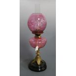 A Victorian oil lamp, having cranberry tinted etched globular shade above a matching cranberry glass