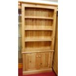 A modern pine freestanding open bookshelf, having twin lower recessed panelled cupboard doors, w.