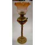 A late Victorian oil lamp having amber tinted frilled etched glass shade above a brass font on a