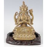 A gilt bronze figure of the Tibetan goddess Chenrezig, in typical seated lotus pose, raised on a