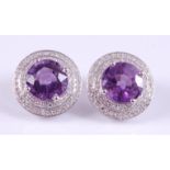 A pair of white metal, amethyst and diamond circular cluster earrings, each featuring a round