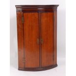 A George III North Country oak and mahogany crossbanded bowfront hanging corner cupboard, the