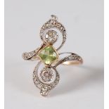 A yellow and white metal peridot and diamond crossover style dress ring, the centre cushion cut