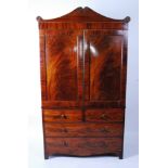 A George IV mahogany linenpress, having a scrolling pediment above a pair of panelled doors,