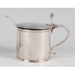 A George II silver mustard pot, of cylindrical form, the hinged cover with a reeded edge, engraved