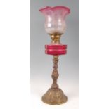 A Victorian brass and cast iron pedestal oil lamp, having cranberry tinted acid etched shade over