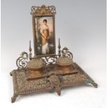 A Victorian brass desk stand, the raised back inset with a porcelain plaque depicting maiden